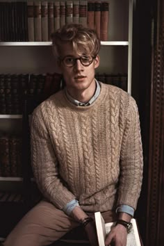 a young man sitting in front of a book shelf