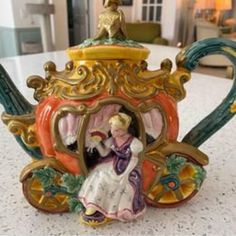 a figurine is sitting on top of a teapot with a woman in it