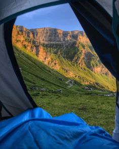 the view from inside a tent looking out at mountains and green grass with blue tarps