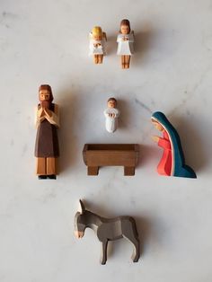 small wooden figurines are arranged on a white surface, including a statue and a horse