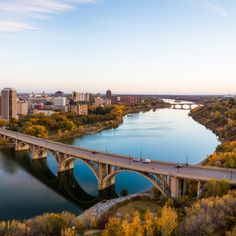 an aerial view of a bridge spanning the width of a river with autumn foliage surrounding it