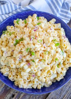 a blue bowl filled with macaroni salad on top of a wooden table next to a striped towel