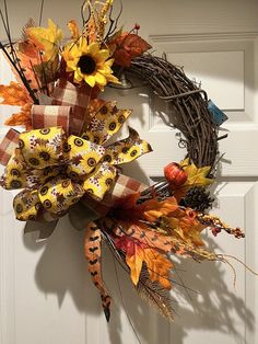 a wreath with sunflowers, leaves and other autumn decorations hanging on a door