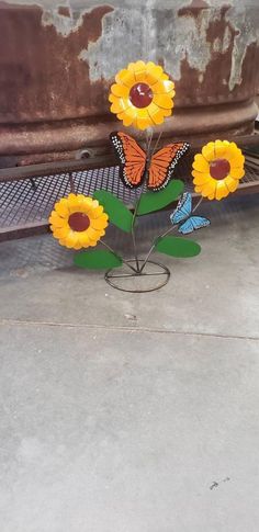 some yellow flowers are sitting in front of a rusted metal car with butterflies on it