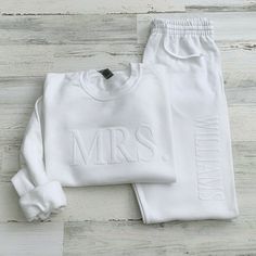 two pieces of white clothing with the word mrs printed on them, sitting on top of a wooden floor