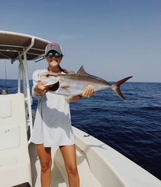 a woman holding a fish on the back of a boat while wearing sunglasses and a hat