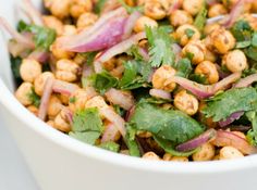 a white bowl filled with chickpeas, onions and cilantro leaves on top of a table