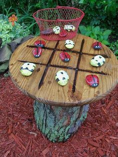 an outdoor table made out of wood with rocks on it and a basket full of cupcakes