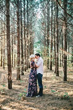 a man and woman standing in the middle of a forest with tall trees behind them