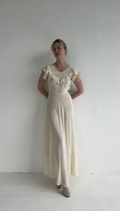 a woman standing in front of a white wall wearing a dress with ruffles