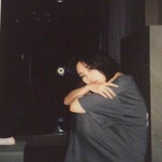 a woman standing in front of a black wall with her arms folded over her chest