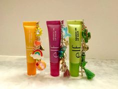 three lip glosses with charms on them sitting next to each other in front of a white wall