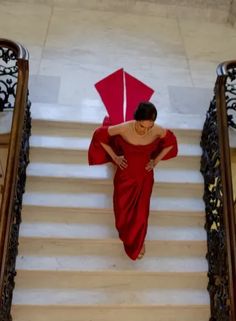 a woman in a red dress is walking down the stairs with an umbrella behind her