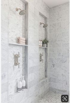 a bathroom with white marble walls and shelves on the wall, along with two shower heads