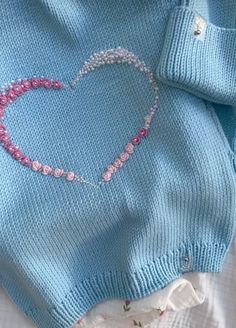 a blue sweater with pink beads and a heart on the front is laying on a bed