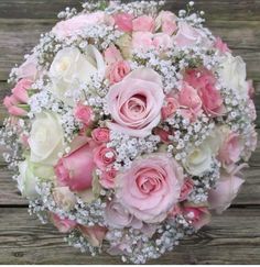 a bouquet of pink and white flowers sitting on top of a wooden table with baby's breath