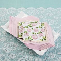 pink napkins with roses on them sitting on a lace tablecloth