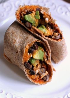 two burritos on a plate with avocado and black beans