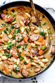 a bowl filled with beans, sausage and carrots on top of a white table