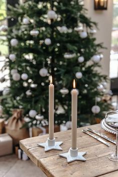 two white candles sitting on top of a wooden table next to a christmas tree in a living room