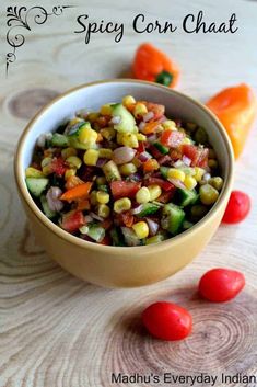 a bowl filled with corn and vegetables on top of a wooden table next to tomatoes