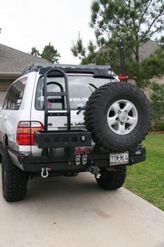 the back end of a white suv parked in front of a house with large tires on it