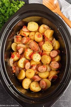 a crock pot filled with cooked potatoes and sausages next to some parsley