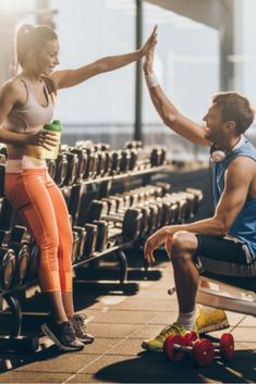 a man and woman sitting on benches in a gym with dumbbells behind them