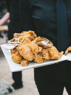 a person holding a plate with fried food on it and tongs in their hand