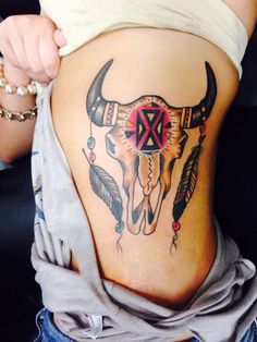 a woman's stomach with an arrow and bull skull tattoo on the bottom side