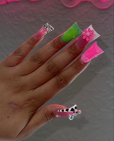 a woman's hand with pink, green and white nail polish on it next to a wall