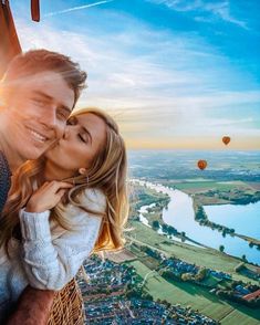 a man and woman are kissing in front of hot air balloons over a river, with the sun shining down on them