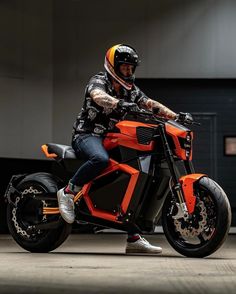 a man riding on the back of an orange motorcycle in a garage next to a building