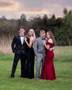 three people in formal wear standing next to each other on the grass with trees in the background