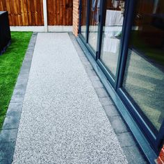 an outdoor walkway with artificial grass in front of a brick building and glass doors on the side