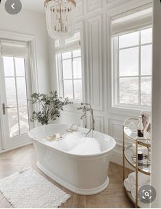 a large white bath tub sitting in a bathroom next to two windows and a chandelier