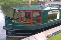 a green boat is docked on the side of the water with plants growing out of it's windows