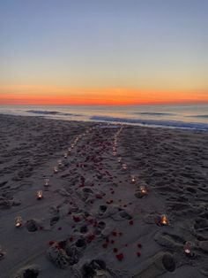 candles are lined up in the sand on the beach as the sun sets over the ocean