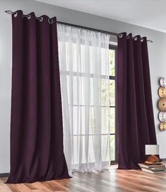 a living room with wooden floors and purple curtains on the windowsill, along with a clock