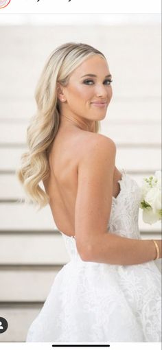 a woman in a white wedding dress holding a bouquet and looking back at the camera