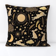 a black and gold pillow with rabbits, stars, and moon on it