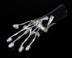 a pair of silver metal gloves on top of a black cloth covered glove with two fingers