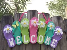 colorful flip flops with flowers and the word welcome hanging on a wooden fence in front of a tree