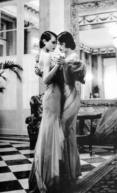 two women in evening gowns embracing each other while standing on a checkered floor