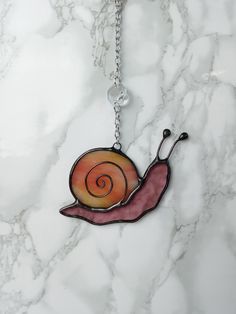 a necklace with a snail on it sitting on top of a marble countertop next to a chain