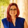 a woman with red hair and glasses smiles for the camera while standing in front of columns