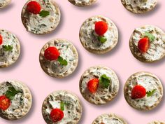 several cookies with cream cheese and fresh strawberries on top, arranged in rows against a pink background