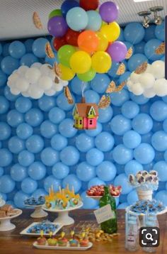 a table topped with lots of balloons and cupcakes next to a wall covered in clouds