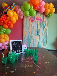 a table topped with balloons and cactus decorations next to a chalkboard sign that says fiesta