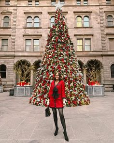 a woman standing in front of a large christmas tree with presents on it's sides